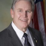 A man in a suit and tie standing in front of an american flag.
