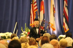 A man playing a bagpipe at an Elks memorial service in front of a crowd of people.