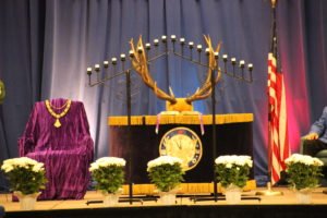 A man sitting on a stage during an Elks memorial service, solemnly holding a deer antler