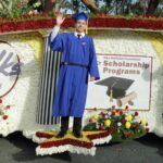 A man in blue graduation outfit standing on the side of a float.