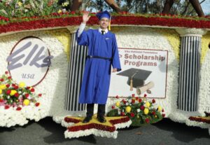A man in blue graduation outfit standing on the side of a float.