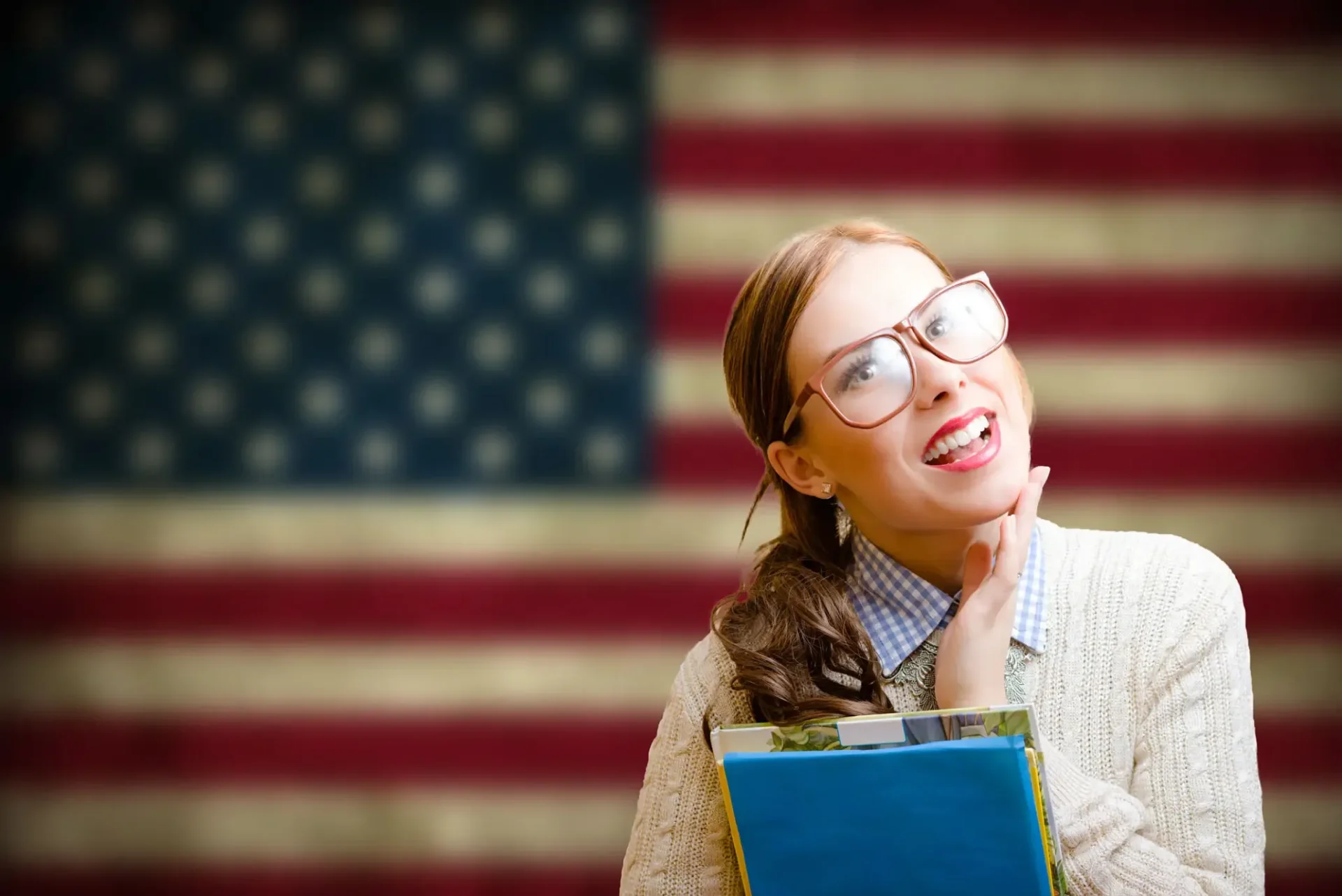Smiling student holding books with American flag background