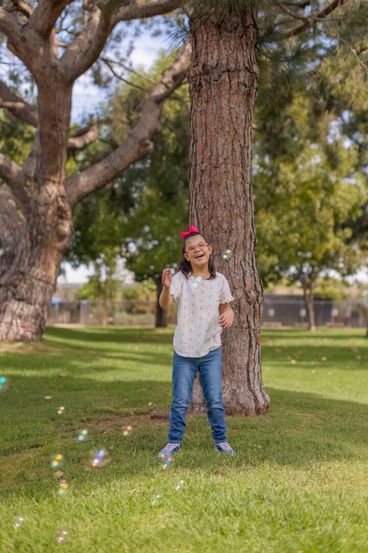 Girl playing with bubbles beneath large tree