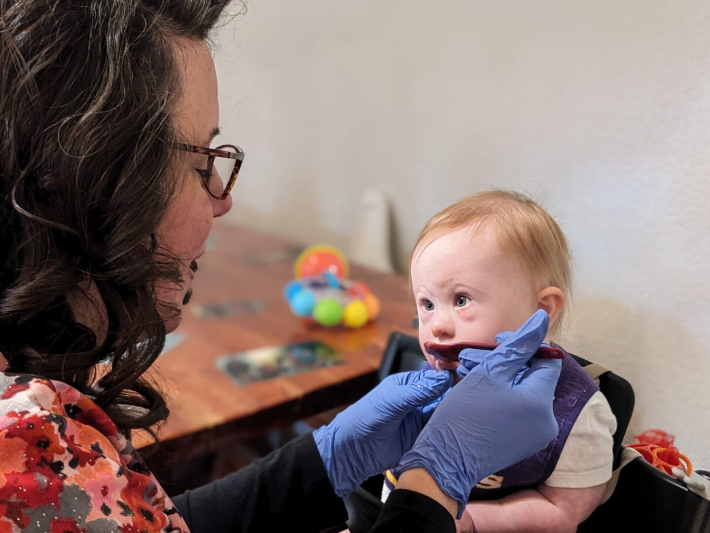Woman wearing gloves examines baby in highchair
