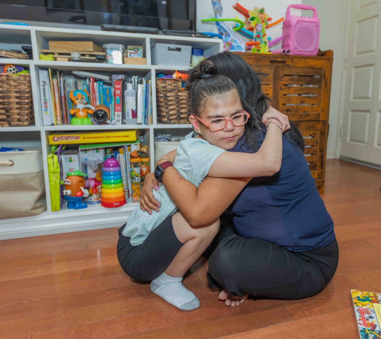 Child with glasses hugging adult in playroom