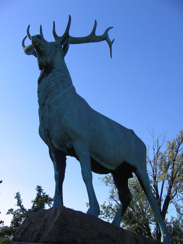 Large bronze elk statue against blue sky